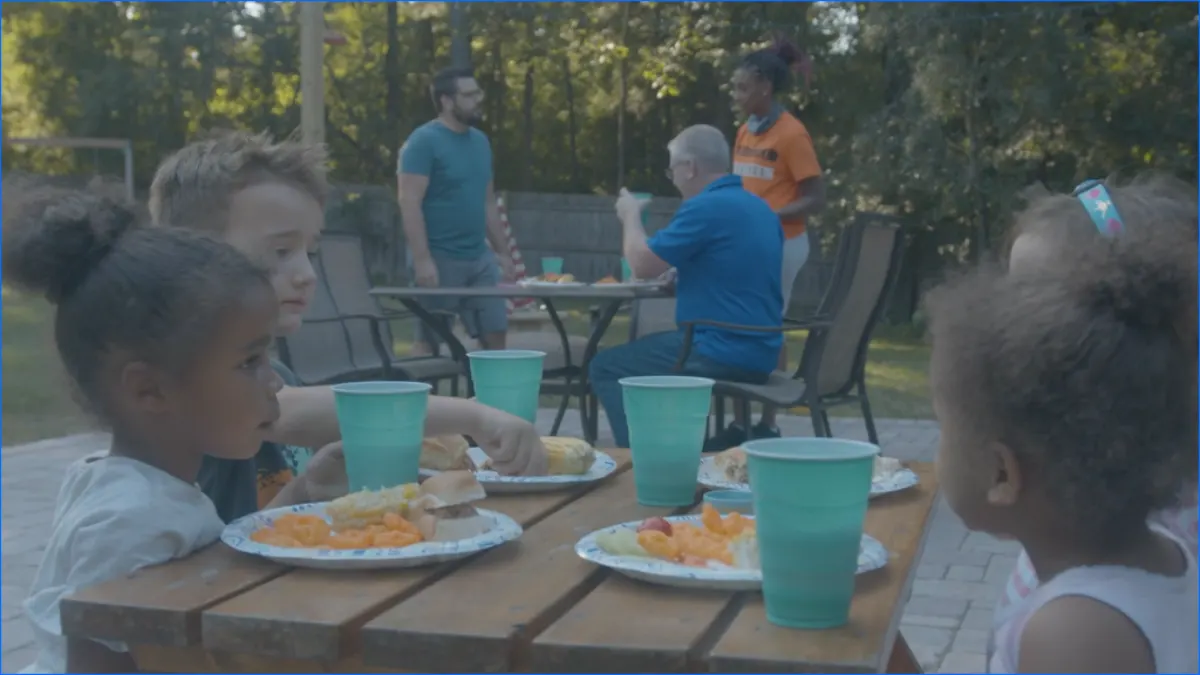 Children sharing a meal outside with a host family.